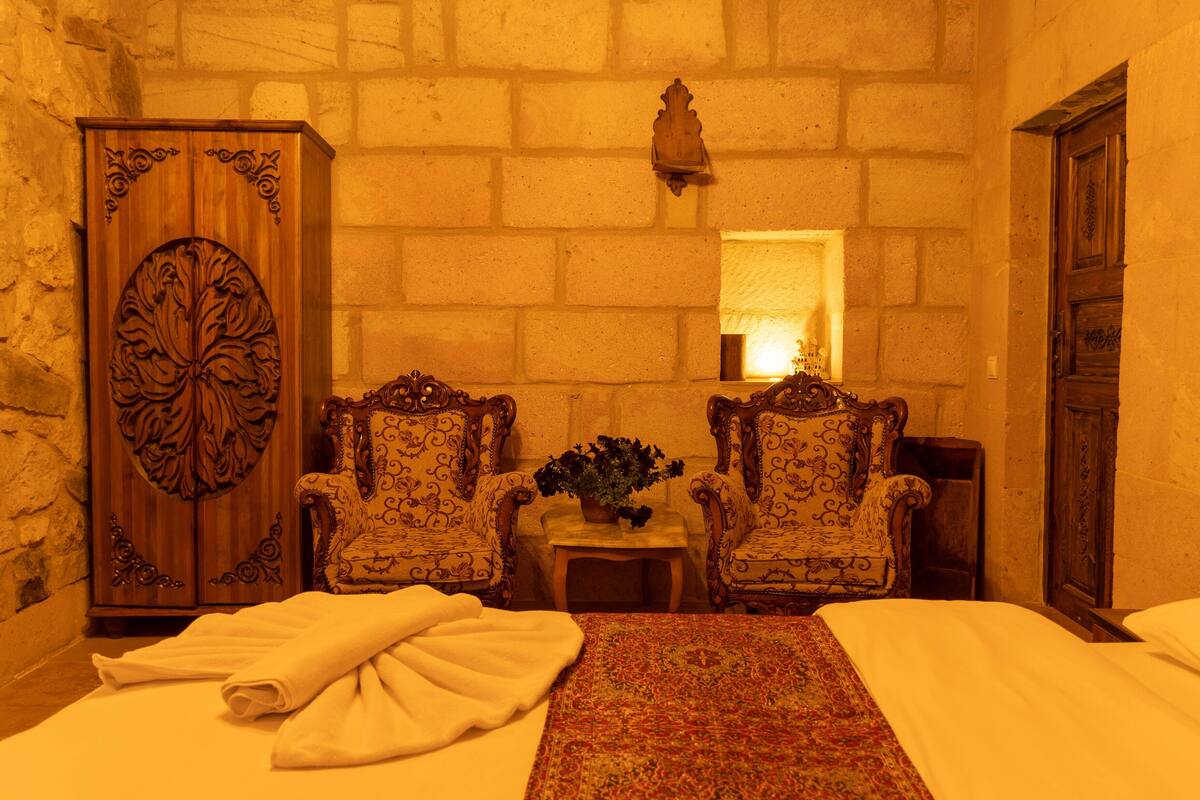 A room with a bed, two ornate armchairs, a wooden cabinet, and a small table with a plant.