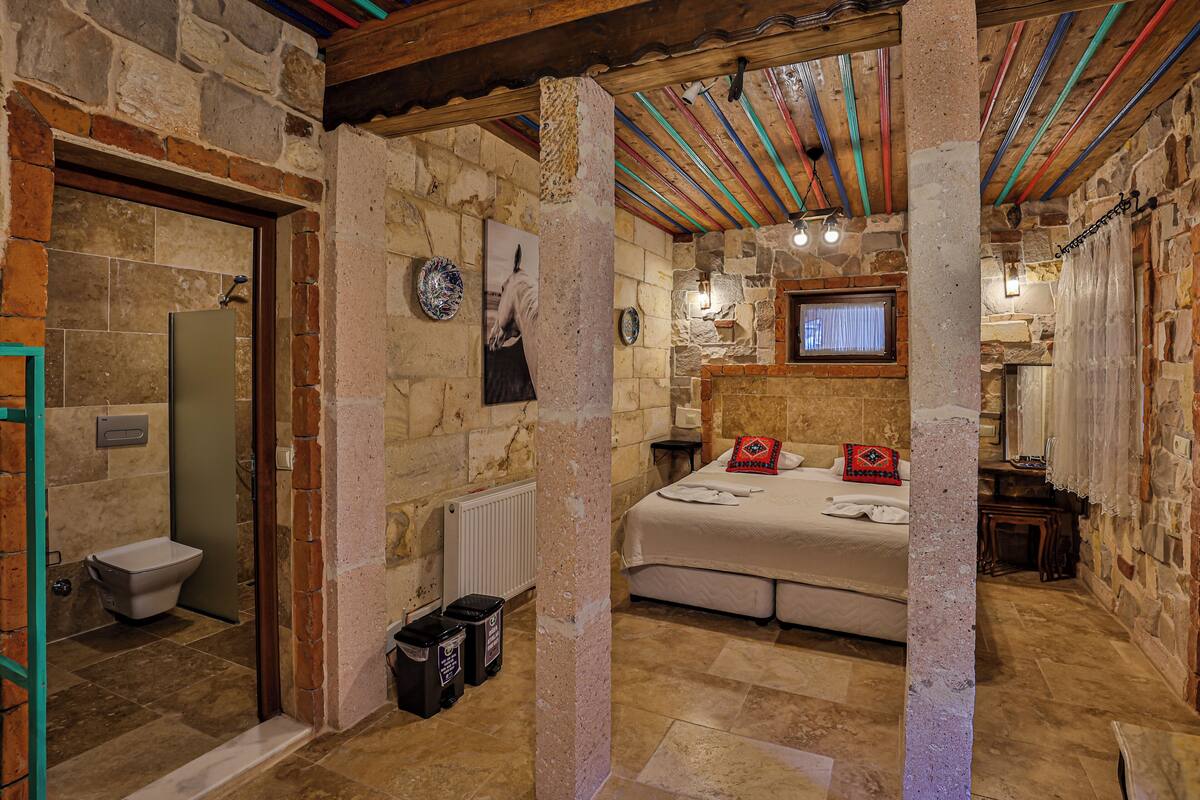A stone-walled bedroom with a bed, a television, and a bathroom with a toilet and shower.