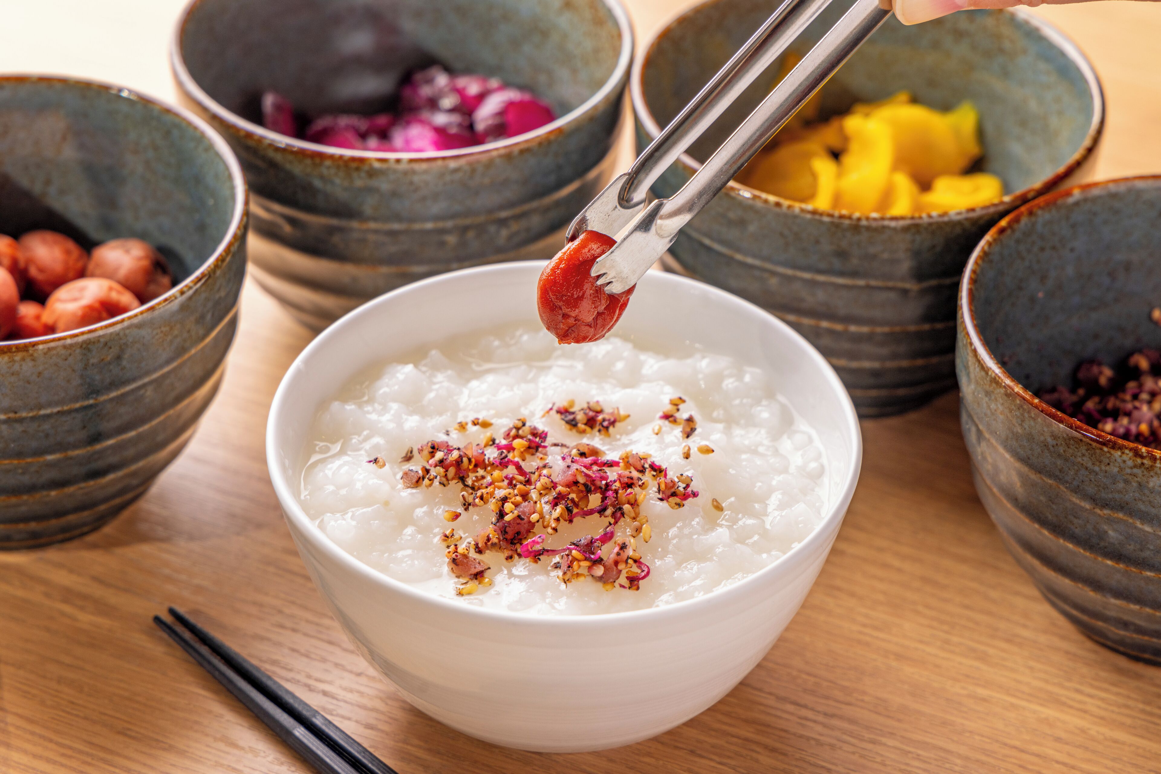 A bowl of white rice with red chili and pink flower garnish, surrounded by bowls of various ingredients.