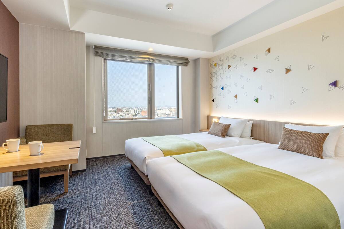 A hotel room with two beds, a desk, and a view of the city.