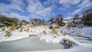 A snow-covered landscape with a pond, trees, and a bridge.