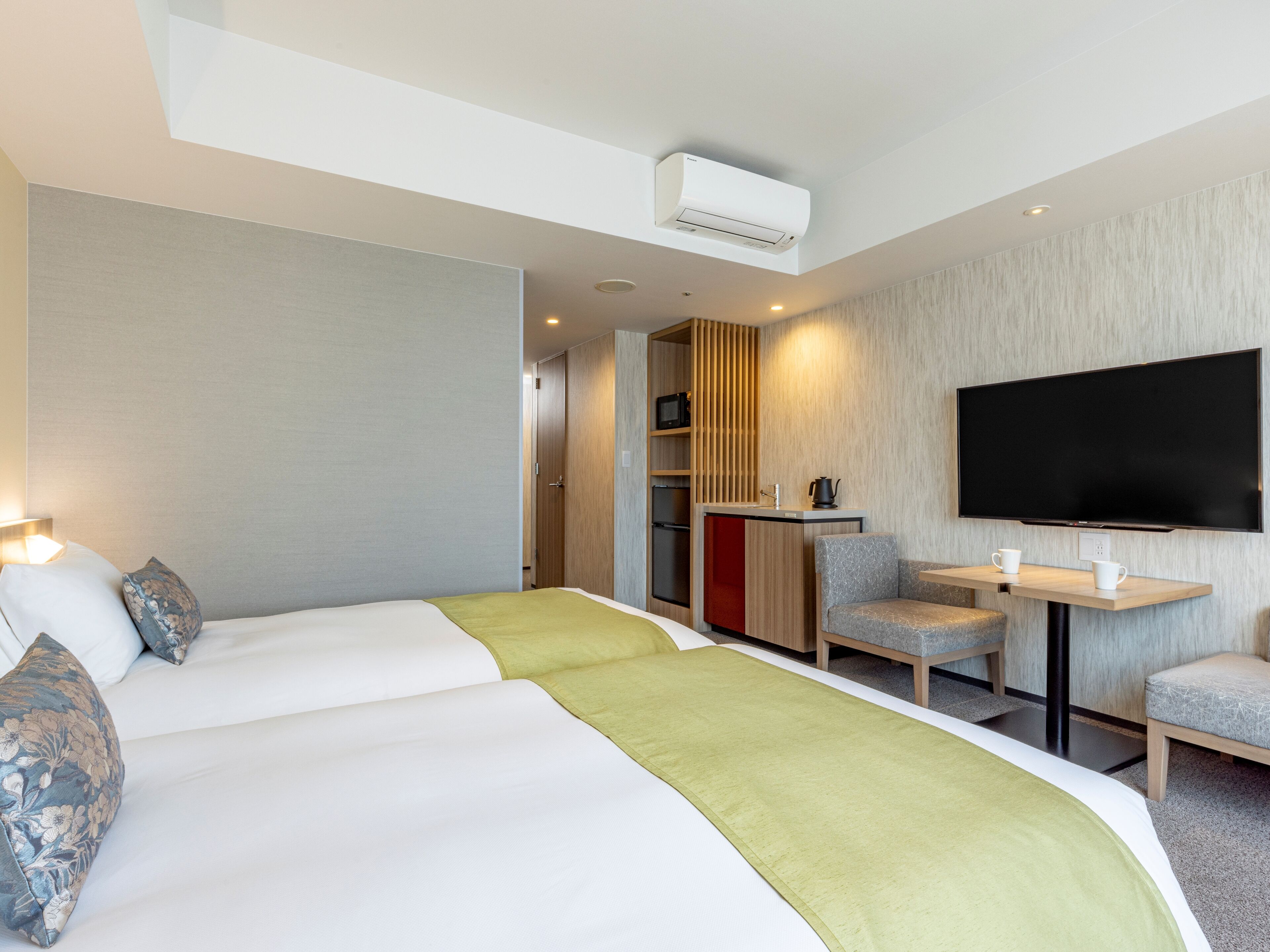 A hotel room with a bed, a TV, a small kitchenette, and a seating area.