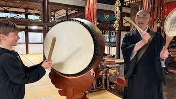 Two individuals playing large drums in a room with traditional decor and wooden furniture.