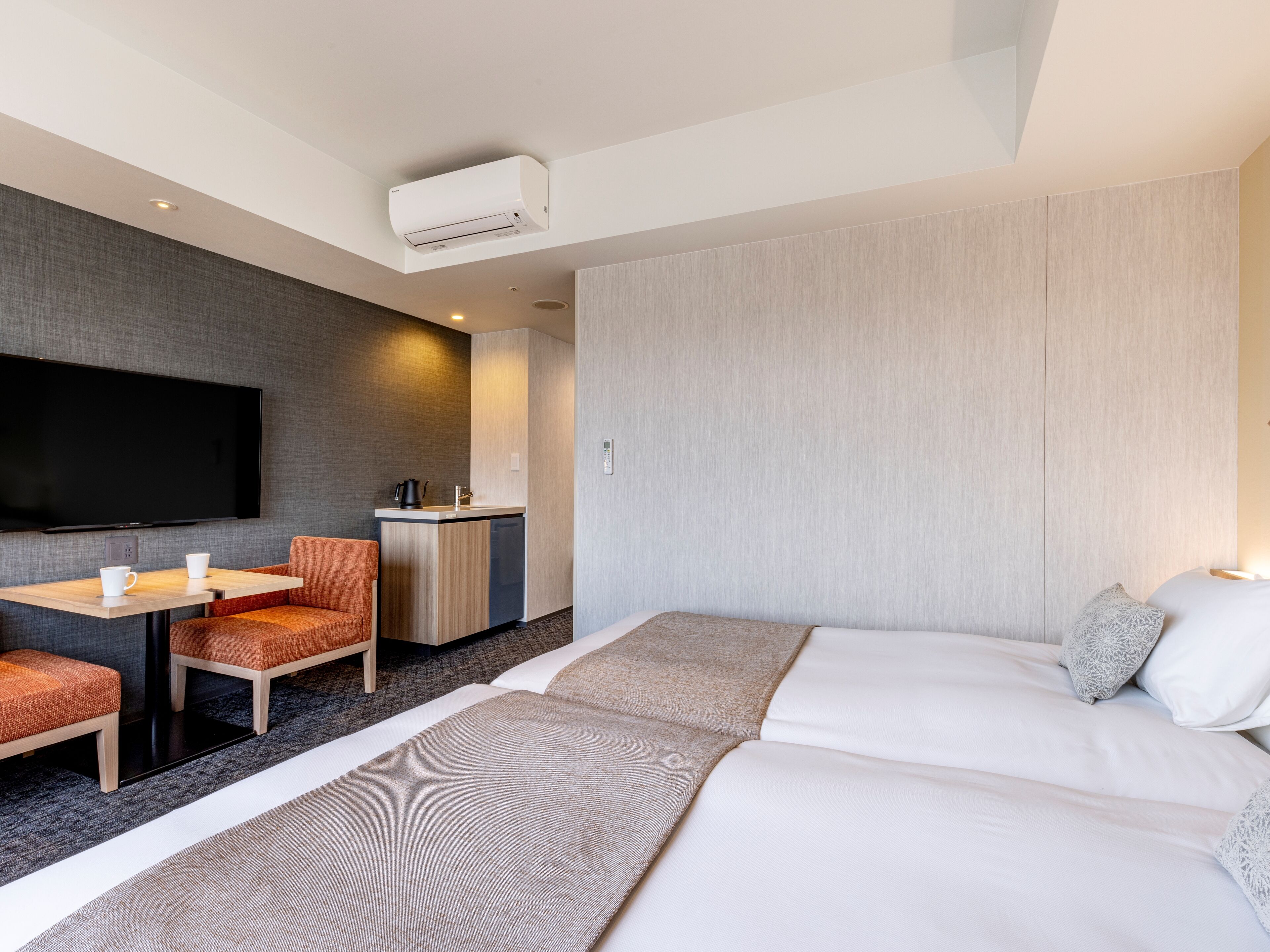 Quarto de hotel moderno com televisão de tela plana, pequeno espaço de cozinha, sofá e cama.