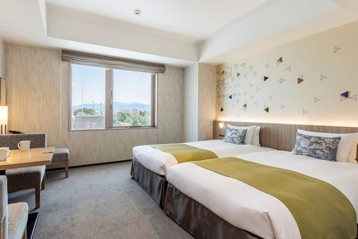 A hotel room with two beds, a desk, a chair, and a large window.