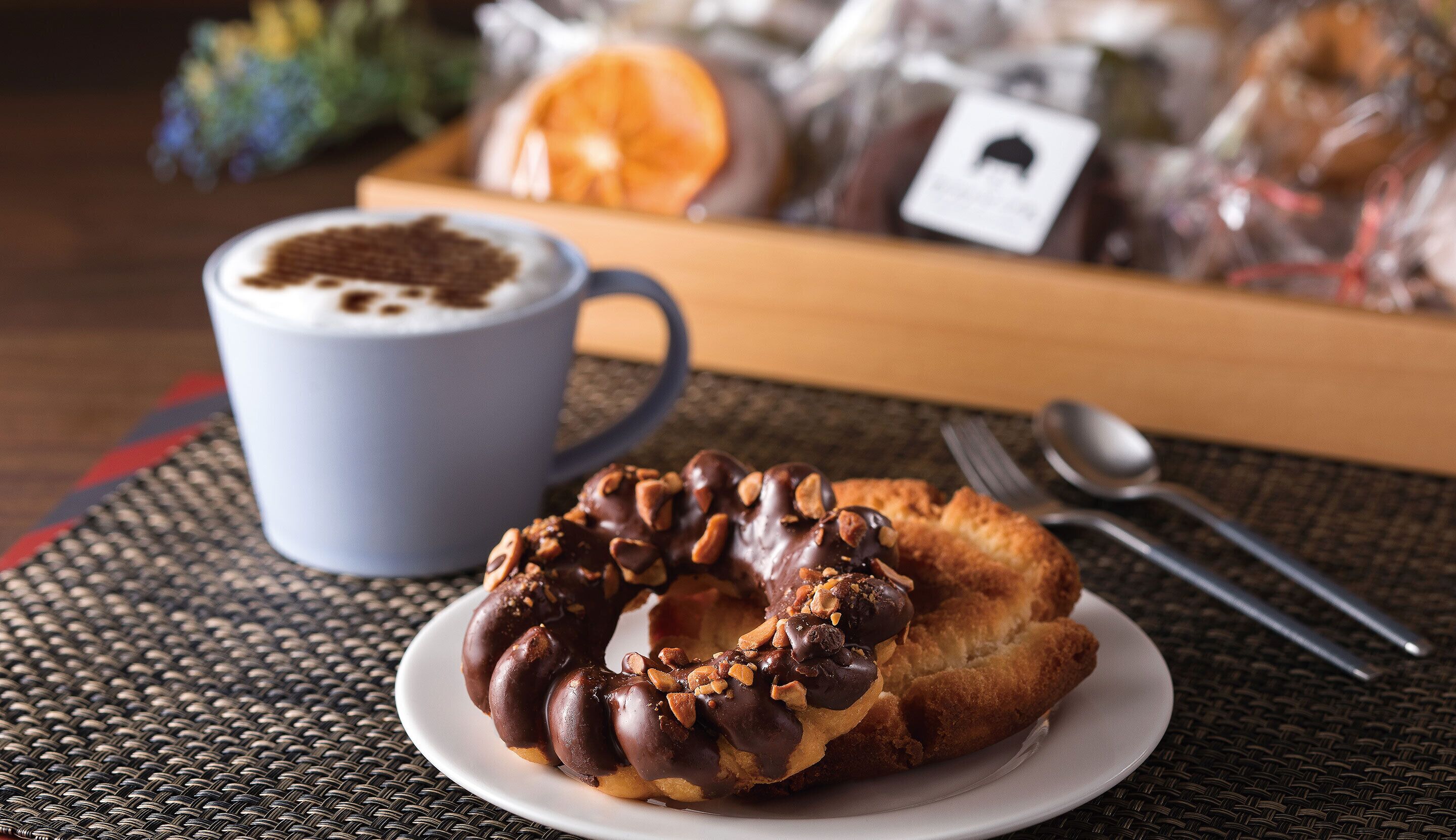 A breakfast setting with a plate of chocolate-covered pastry and a cup of coffee on a woven placemat.