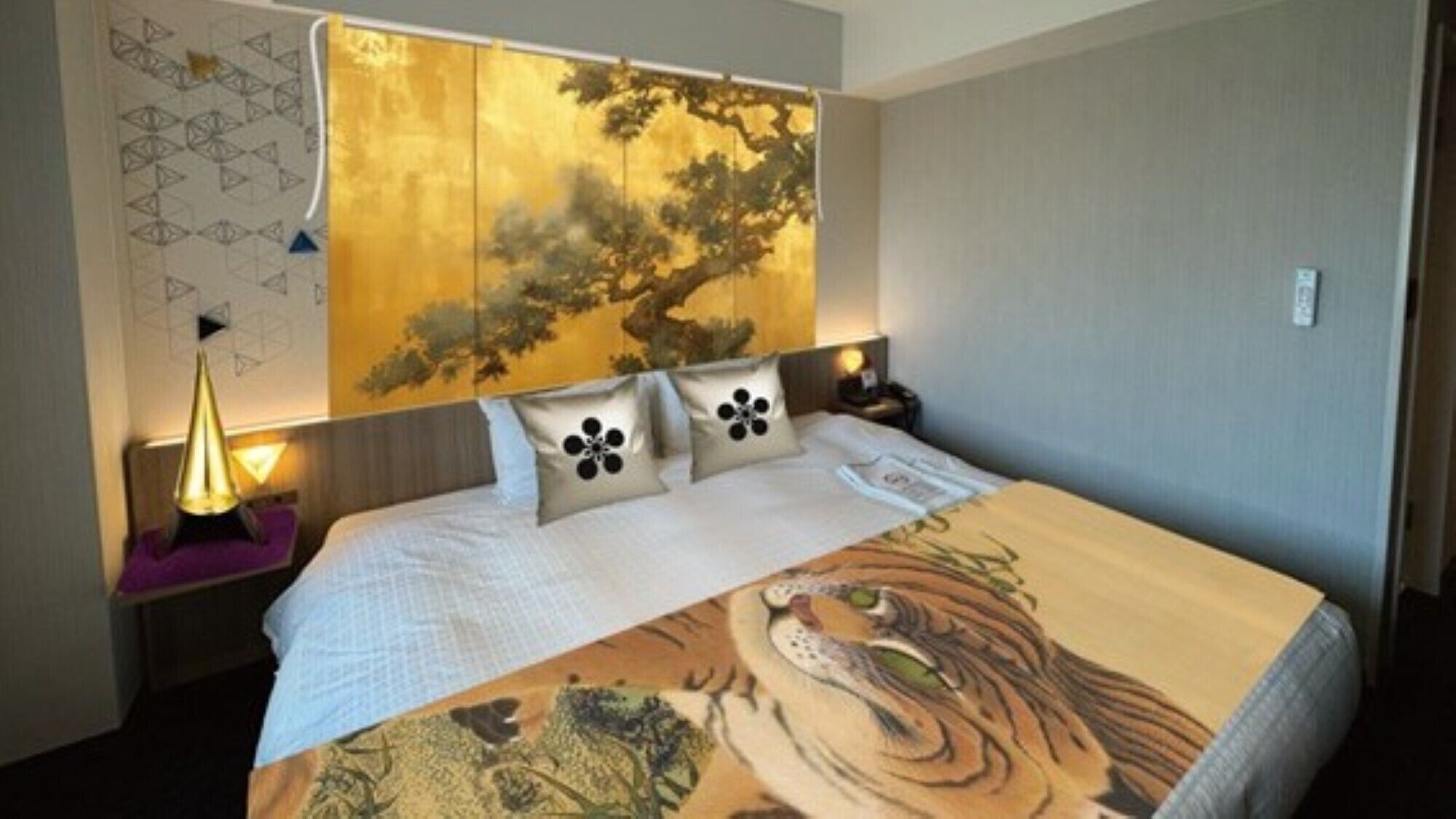 A hotel room with a bed, a headboard with a tree design, and a nightstand with a lamp.