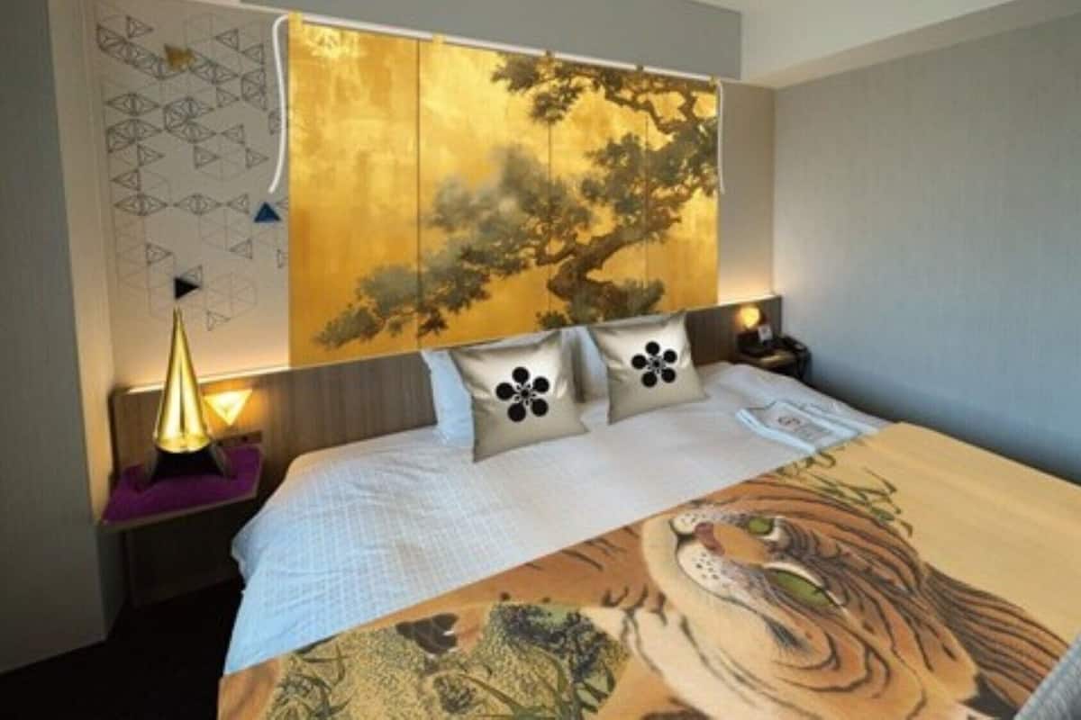A hotel room with a bed, a headboard with a tree design, and a nightstand with a lamp.