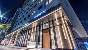 Un hotel modern amb un distintiu senyalitzador de "TOKYU STAY", grans finestres de vidre i una entrada ben il·luminada.