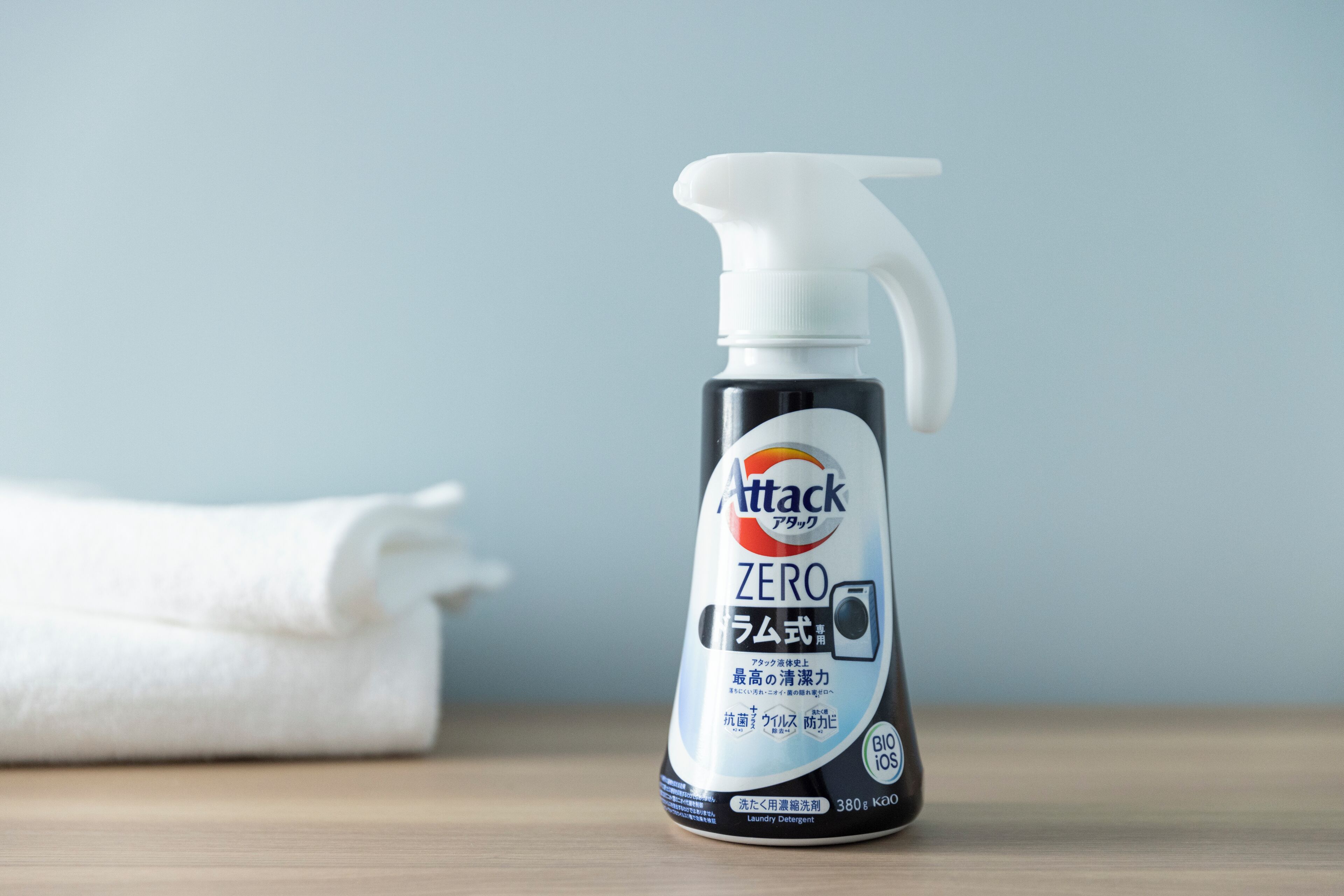 A bottle of Attack Zero laundry detergent on a wooden surface with a white towel in the background.