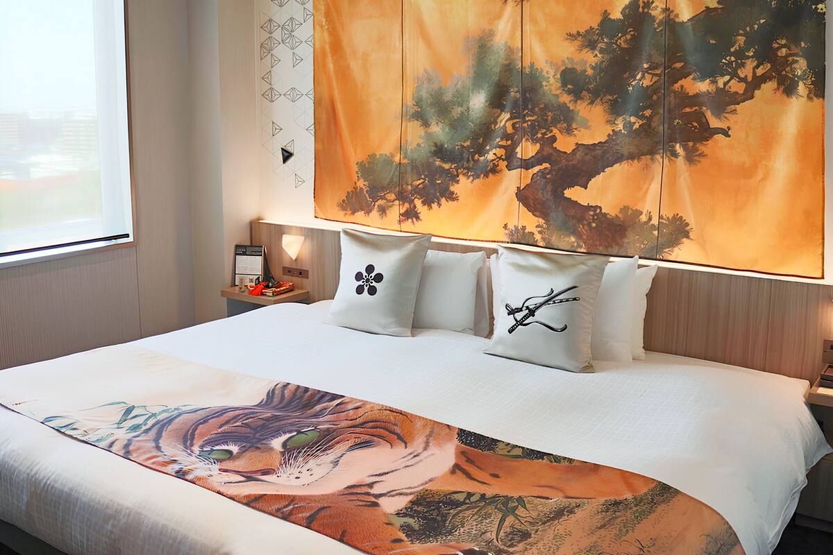 A hotel room with a large bed, a nightstand, a lamp, and a window with curtains.