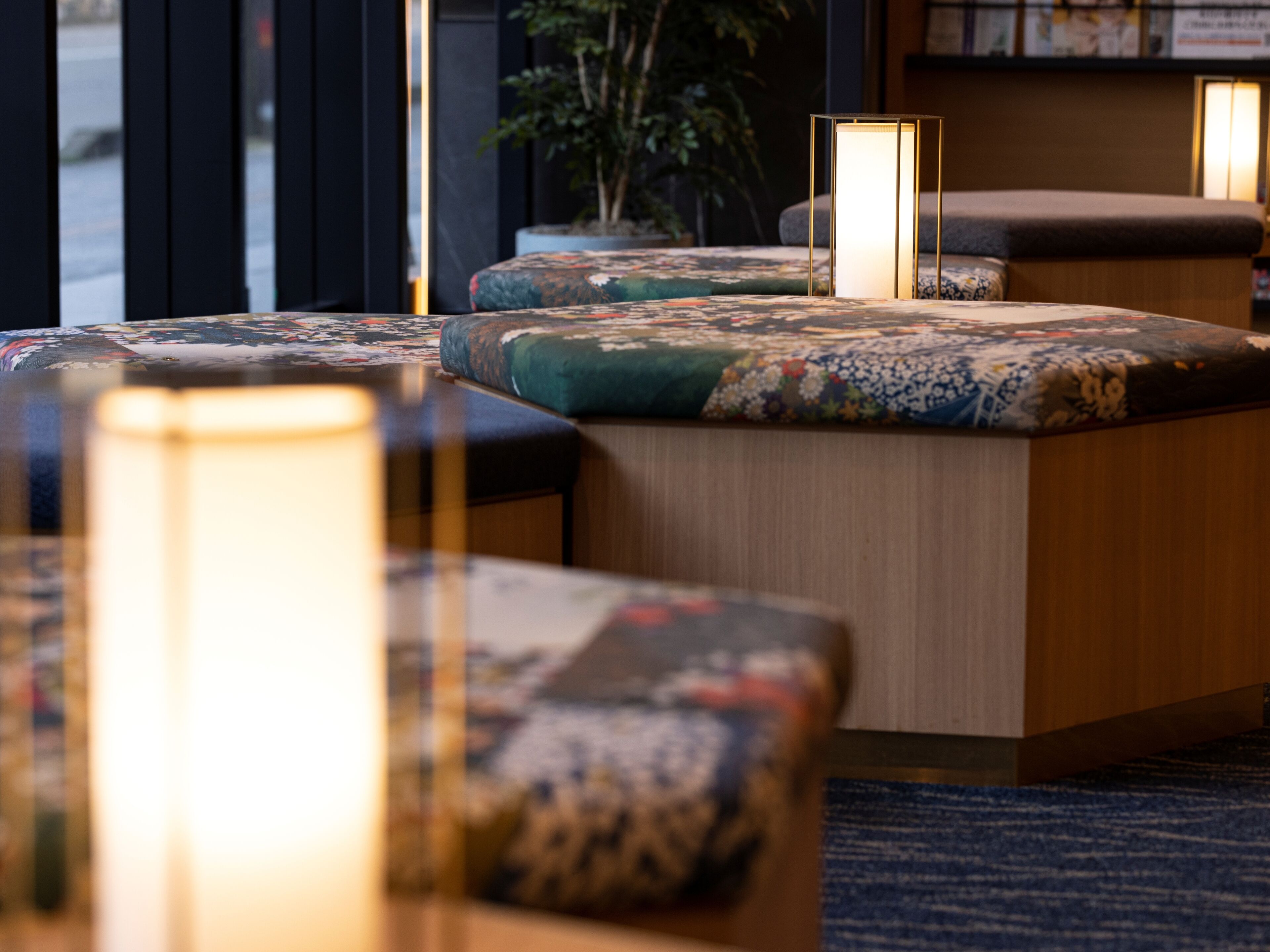 Eine moderne Hotelhalle mit Sitzgelegenheit, darunter eine Holzbank mit Blumenkissen, eine Stehlampe und ein Blumentopf.