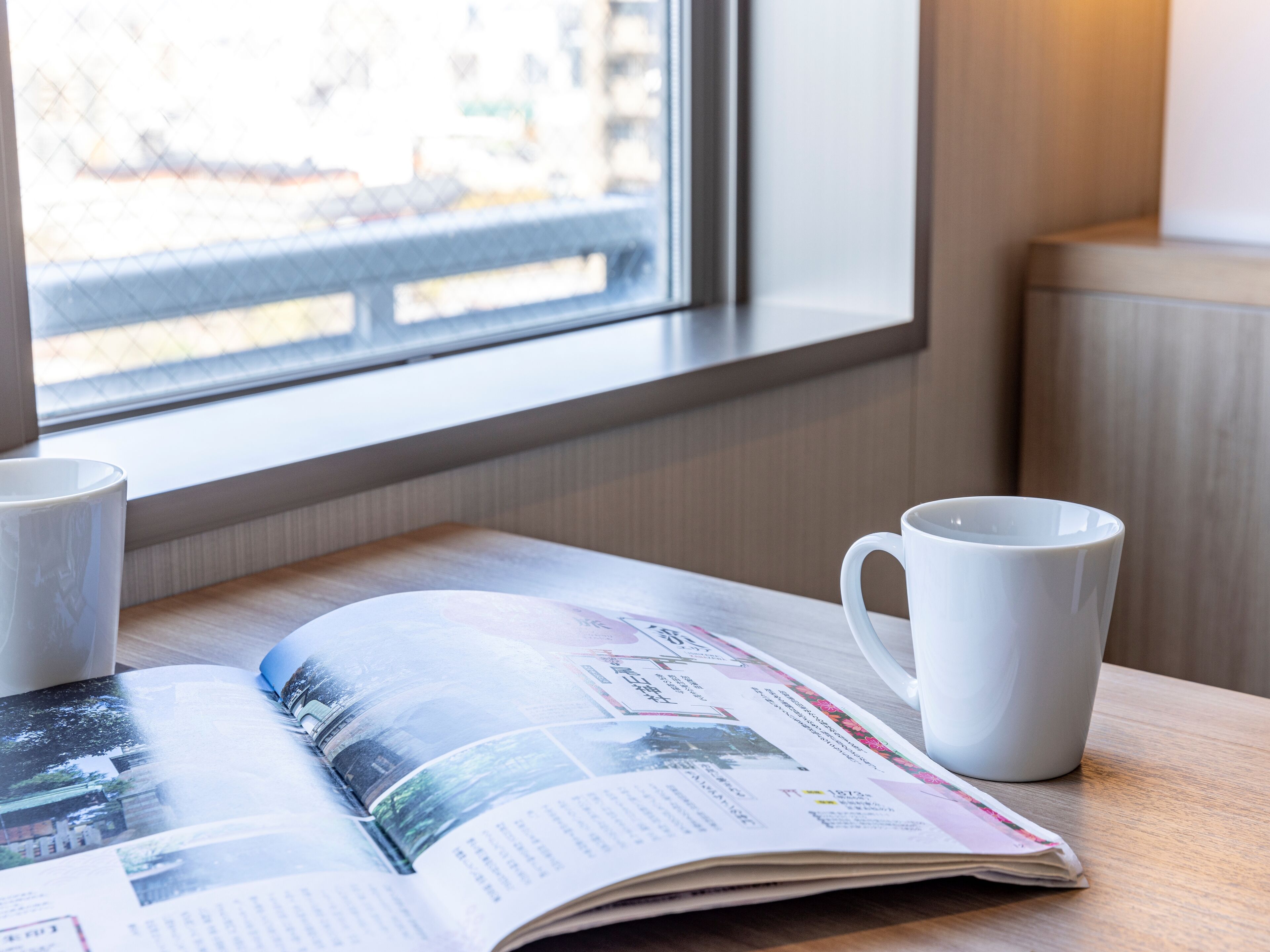 A table with a magazine and two white mugs.