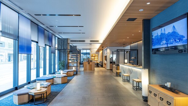 Un vestíbul d'hotel modern amb una llarga recepció, zona de seients i grans finestres que donen vistes al carrer.