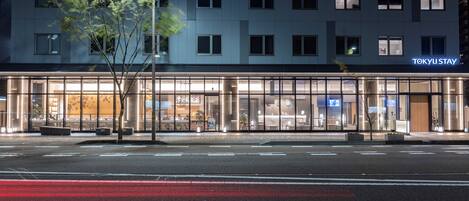 A modern hotel with a glass facade, a sign reading "TOKYU STAY", and a tree in front.