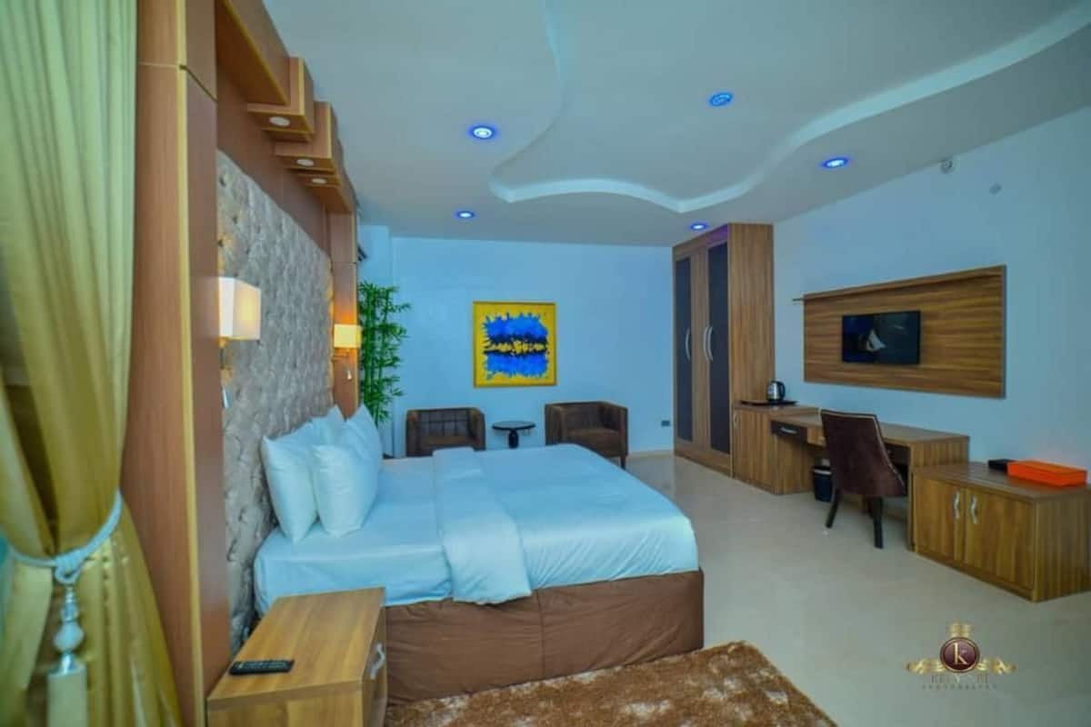 A modern hotel room with a large bed, a desk, a TV, and a painting on the wall.