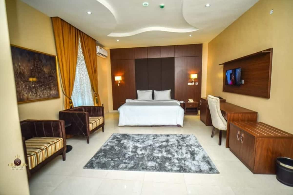 A hotel room with a bed, a desk, a chair, a TV, and a painting on the wall.