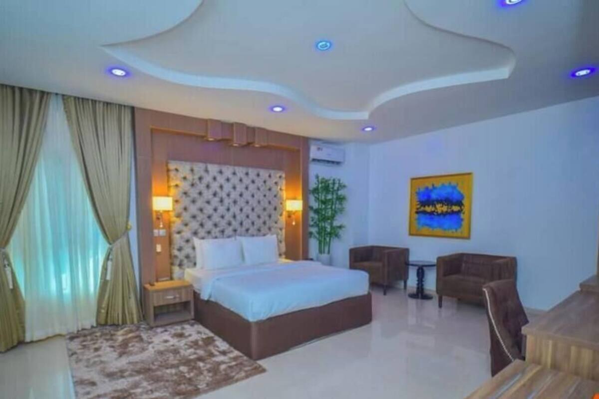 A modern hotel room with a large bed, a desk, a chair, and a sofa.