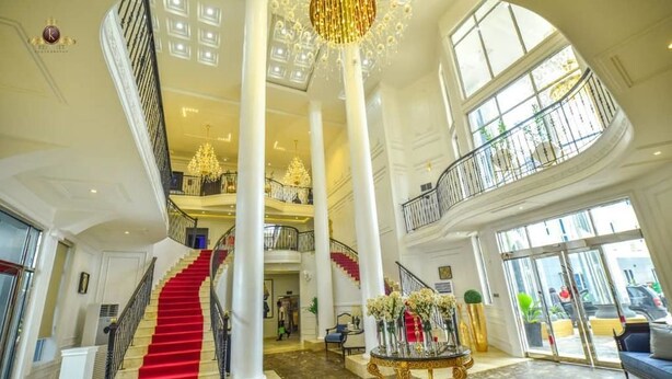 A grand lobby with a red carpeted staircase, high ceilings, and a chandelier. - JJ Mas Hotel (Owerri)