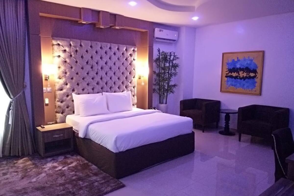 A bedroom with a large bed, bedside tables, a nightstand, a potted plant, a small table, and a chair.