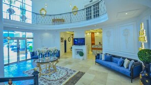 A spacious lobby with a high ceiling, a grand staircase, a pool area, and a seating area with blue sofas. - JJ Mas Hotel (Owerri)