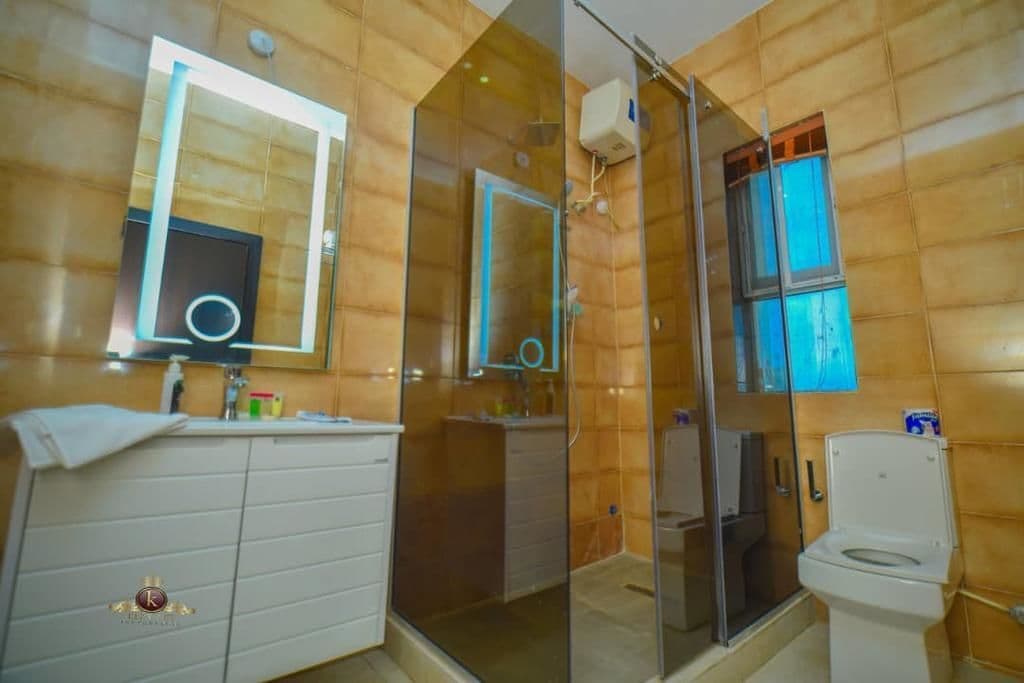 Un bany amb plat de dutxa de vidre, un lavabo blanc amb mirall i un vàter.
