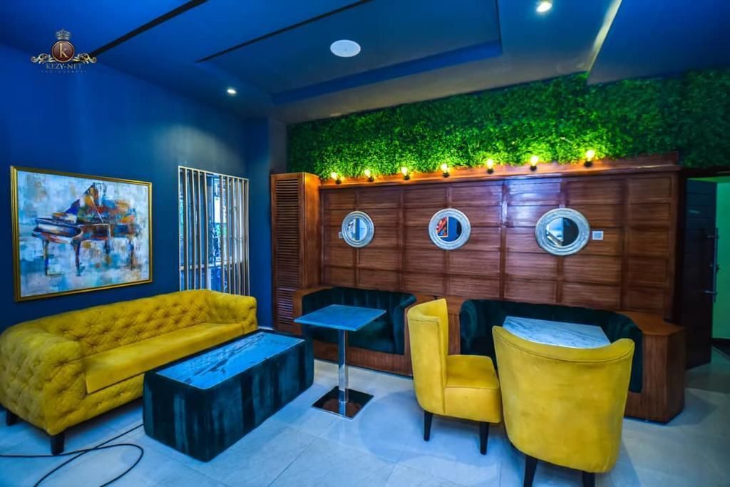 A modern lounge area with a yellow sofa, a round wooden wall with mirrors, and a green wall with lights.