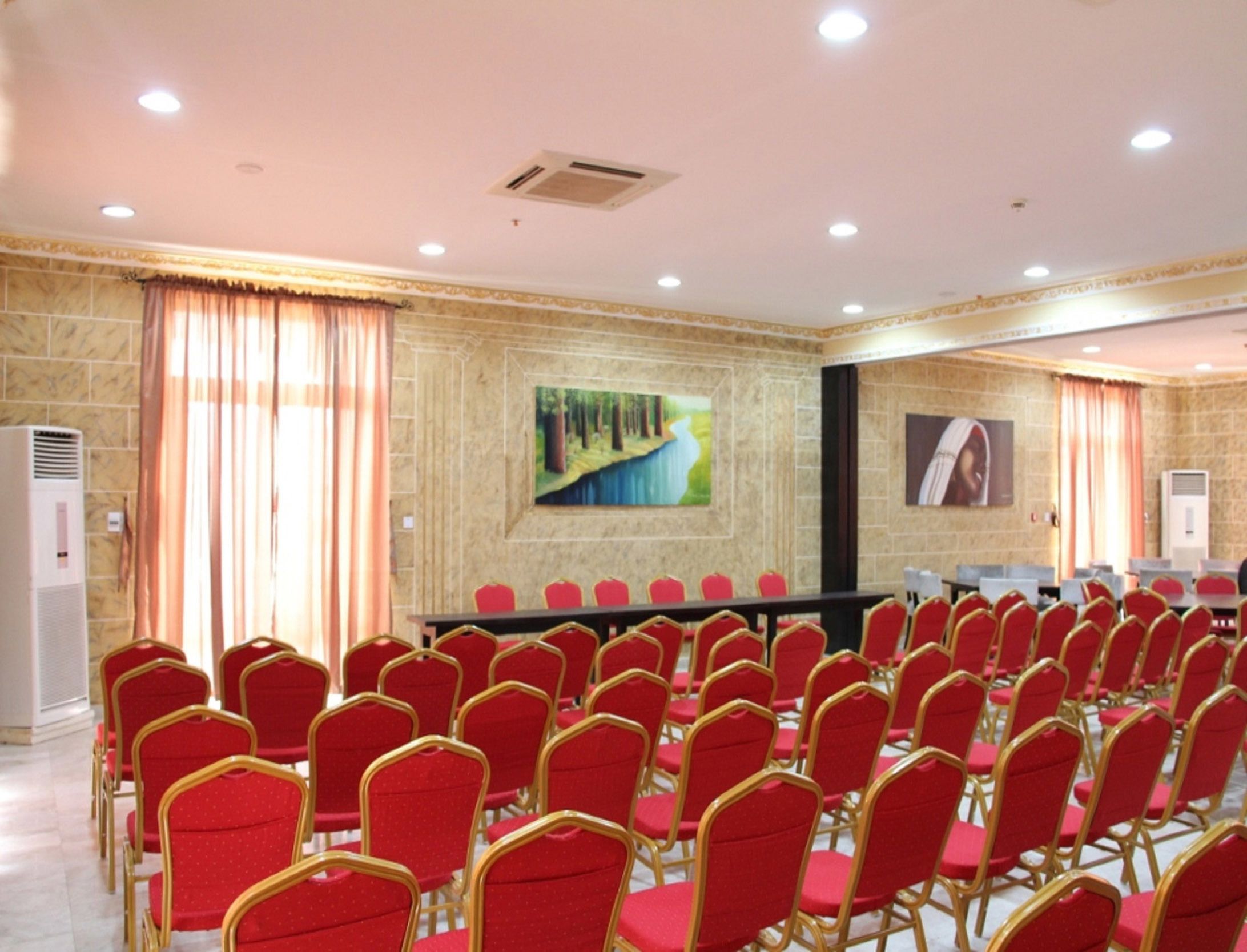 A conference room with rows of red chairs, a long table, and two paintings on the walls.