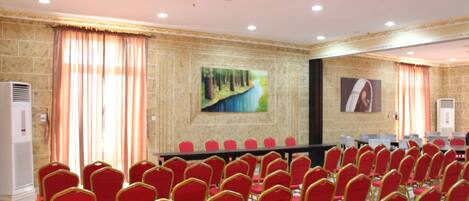 A conference room with rows of red chairs, a long table, and two paintings on the walls.