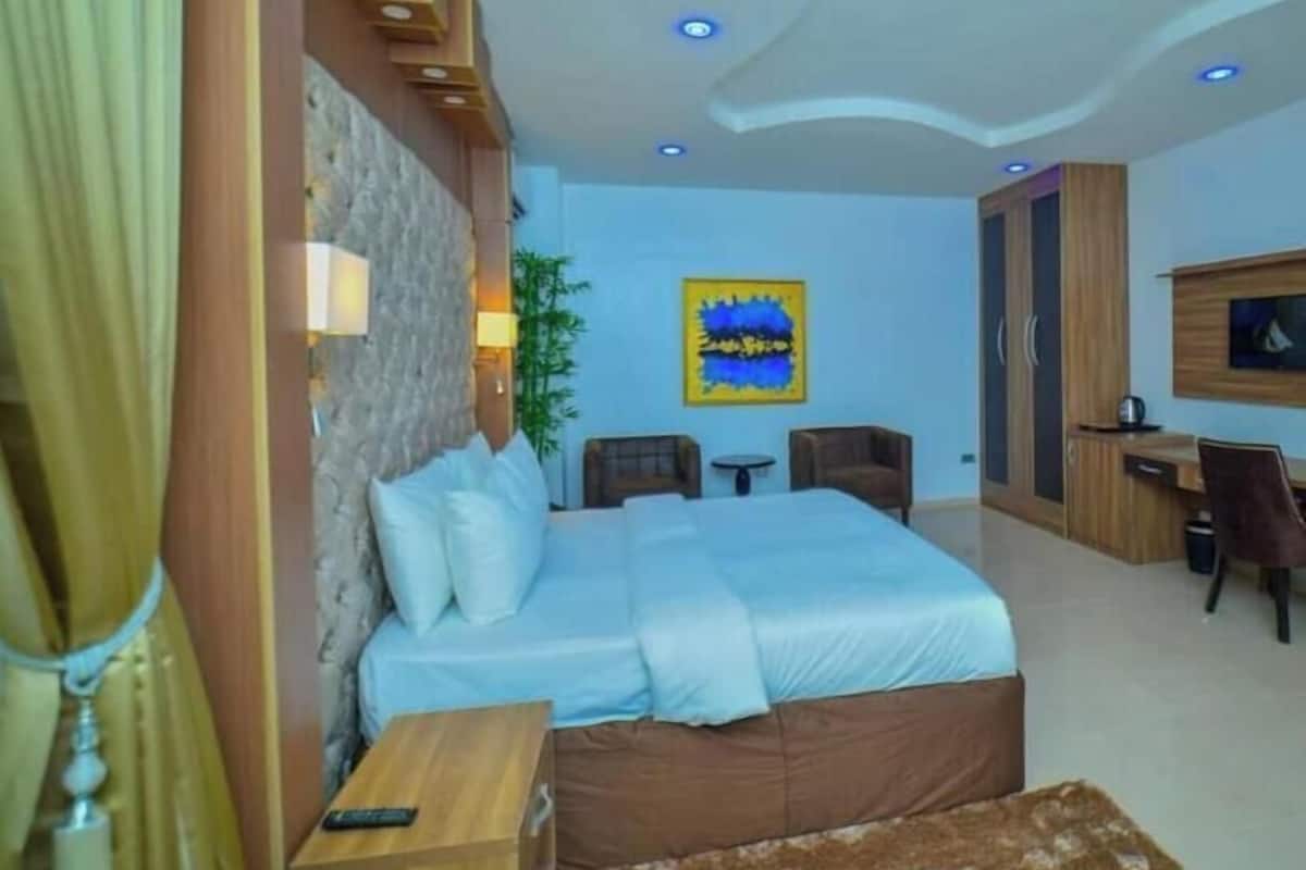 A bedroom with a bed, a desk, a chair, a lamp, and a painting on the wall.
