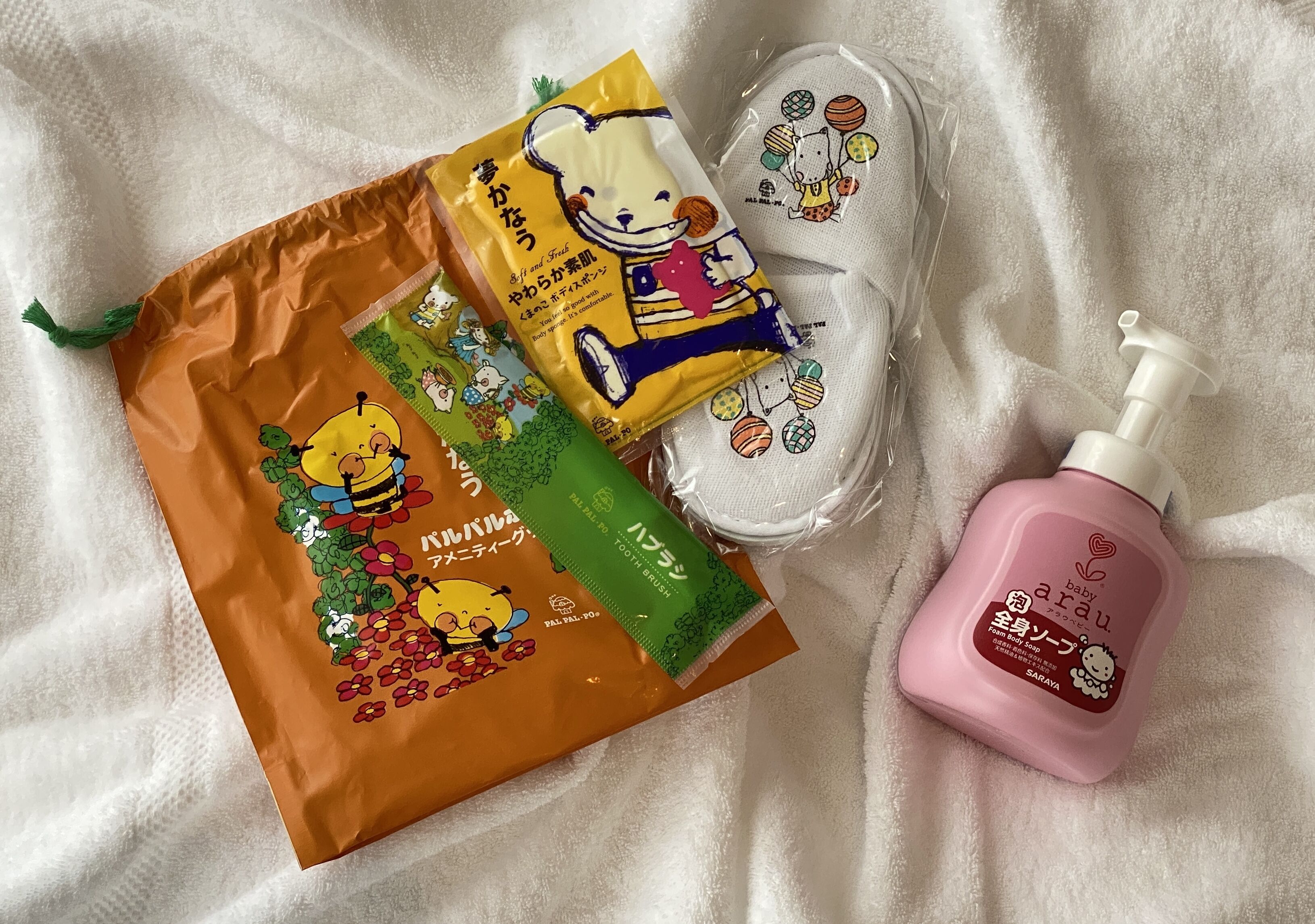 A white towel, a pink bottle, and two bags with cartoon characters.