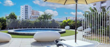 An outdoor patio with a pool, seating, and a large umbrella.