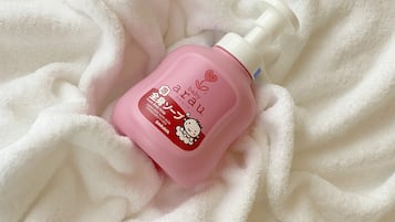 A pink bottle of baby soap with a pump dispenser on a white textured surface.