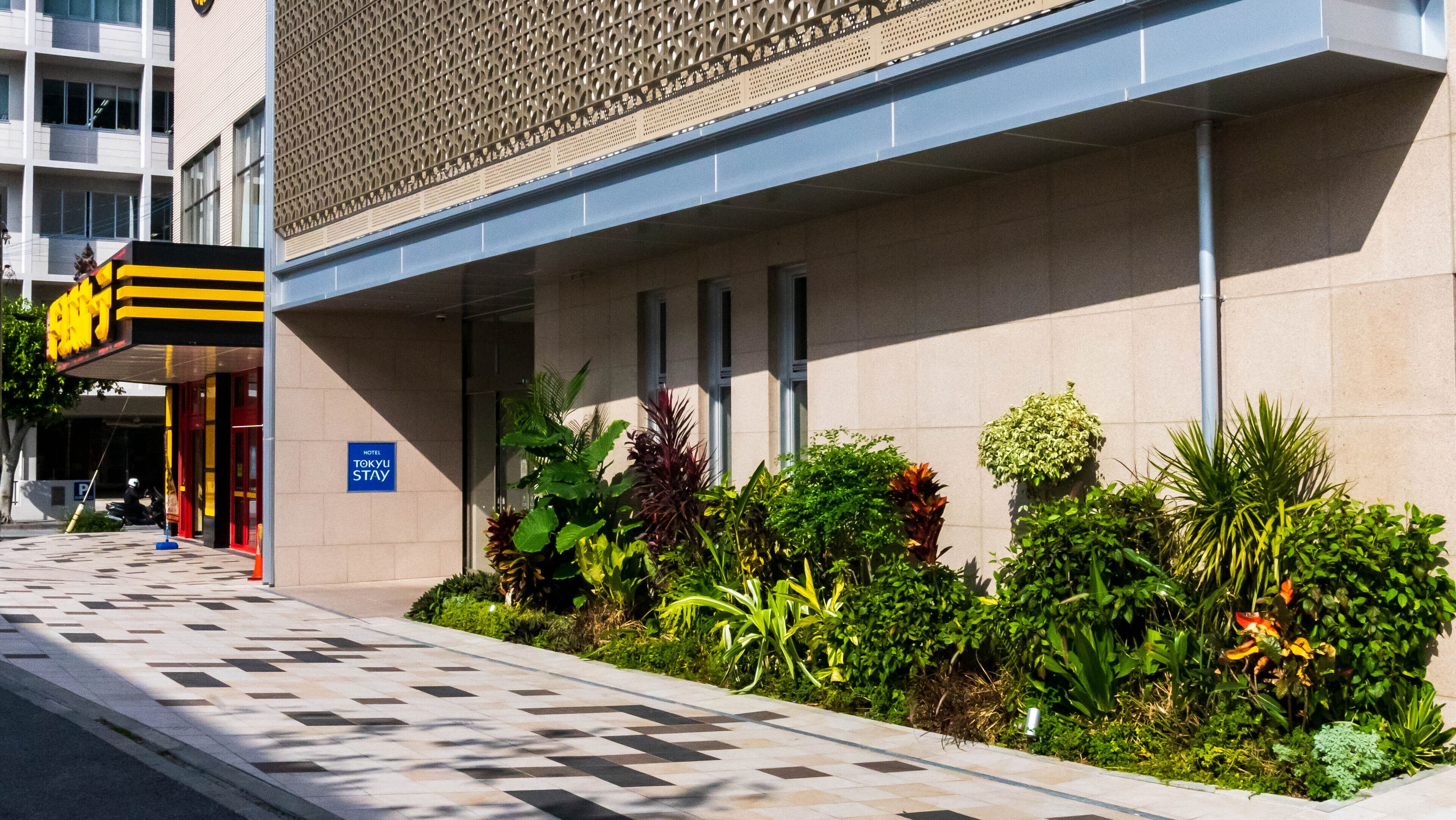 A hotel entrance with a sign for 'Tokyo Stay' and a tiled pathway leading to the entrance.