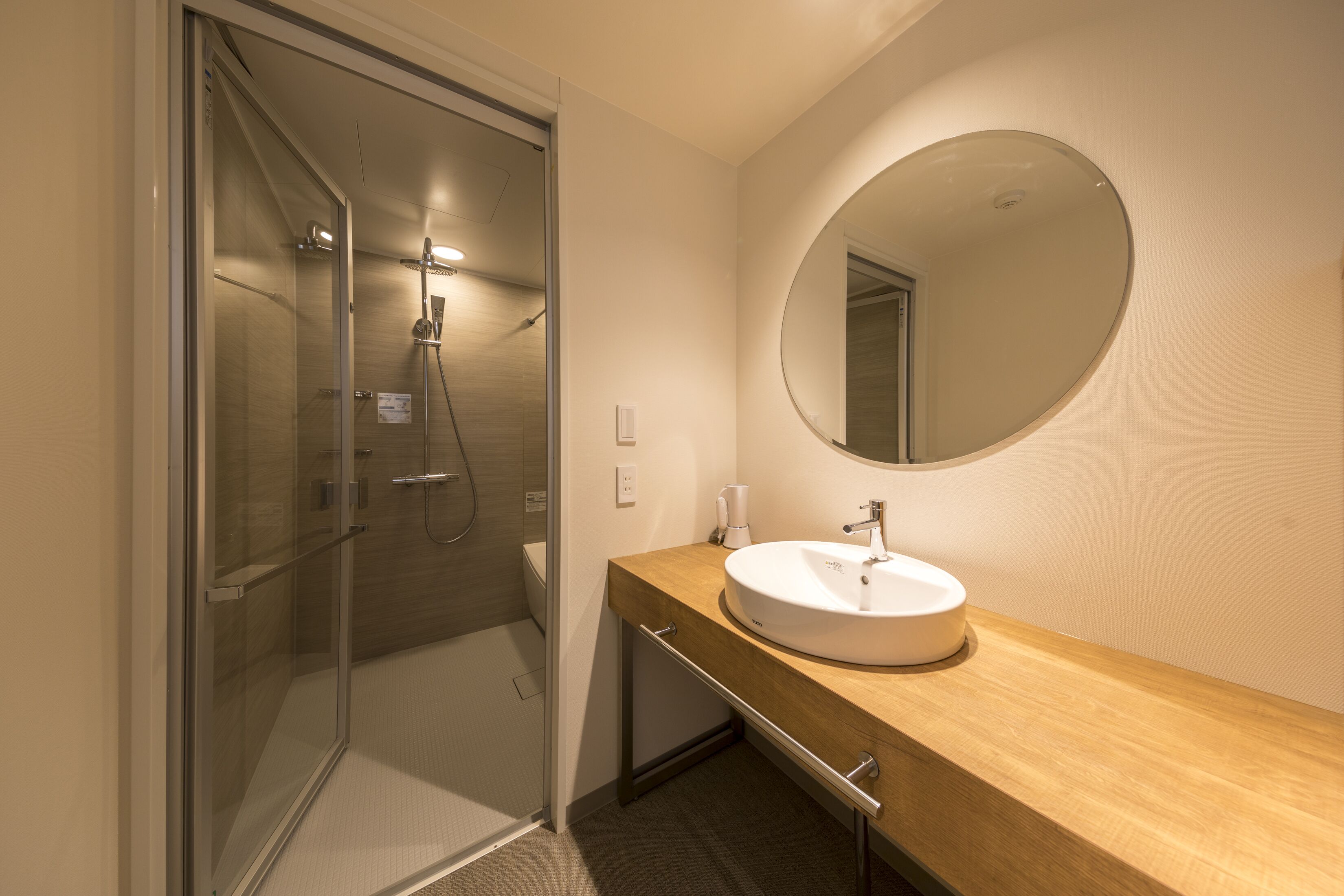 A modern bathroom with a glass shower enclosure, a wooden vanity with a sink, and a round mirror.