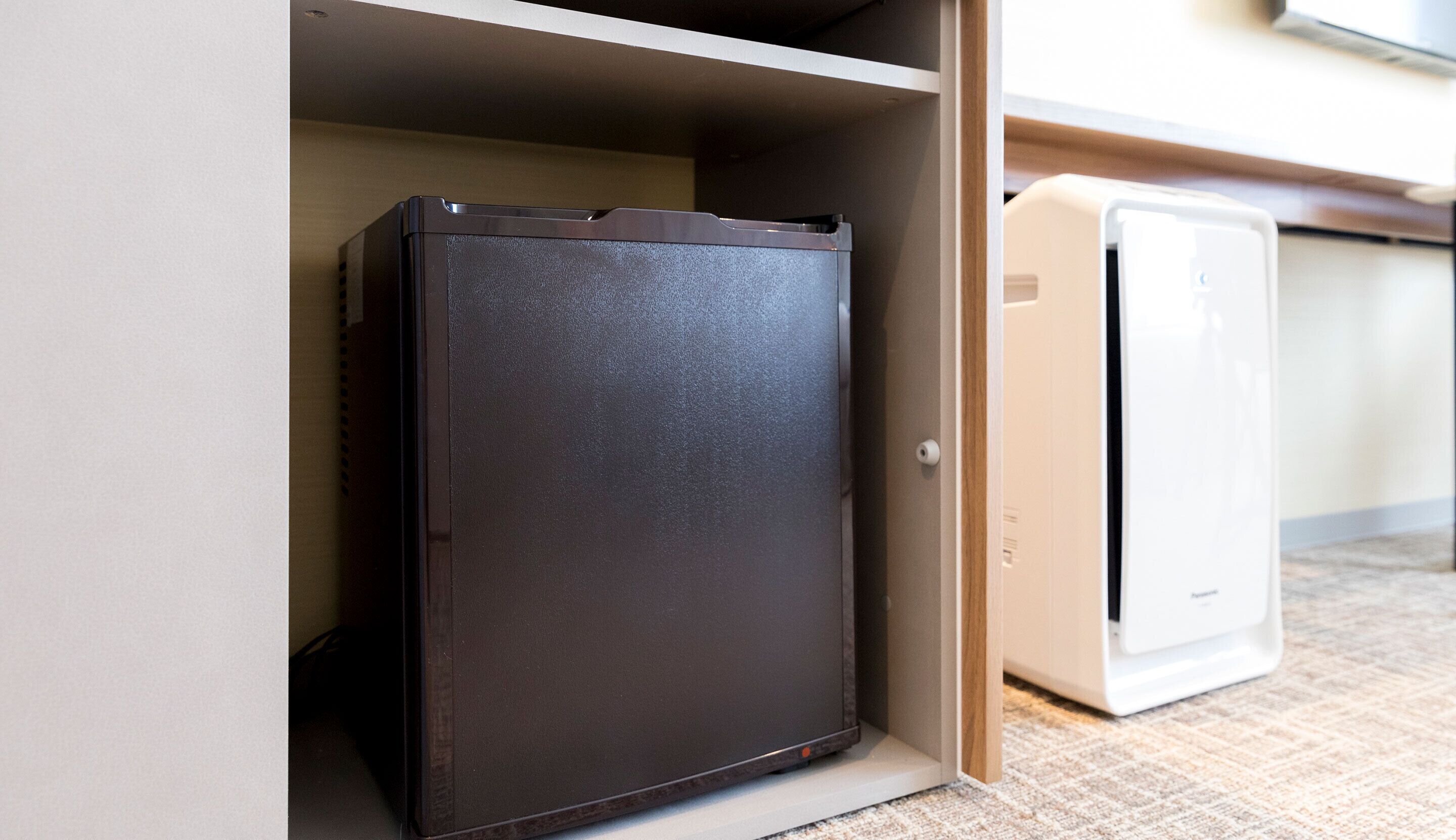 A compact refrigerator and a microwave in a kitchen with a beige countertop and a wooden cabinet.