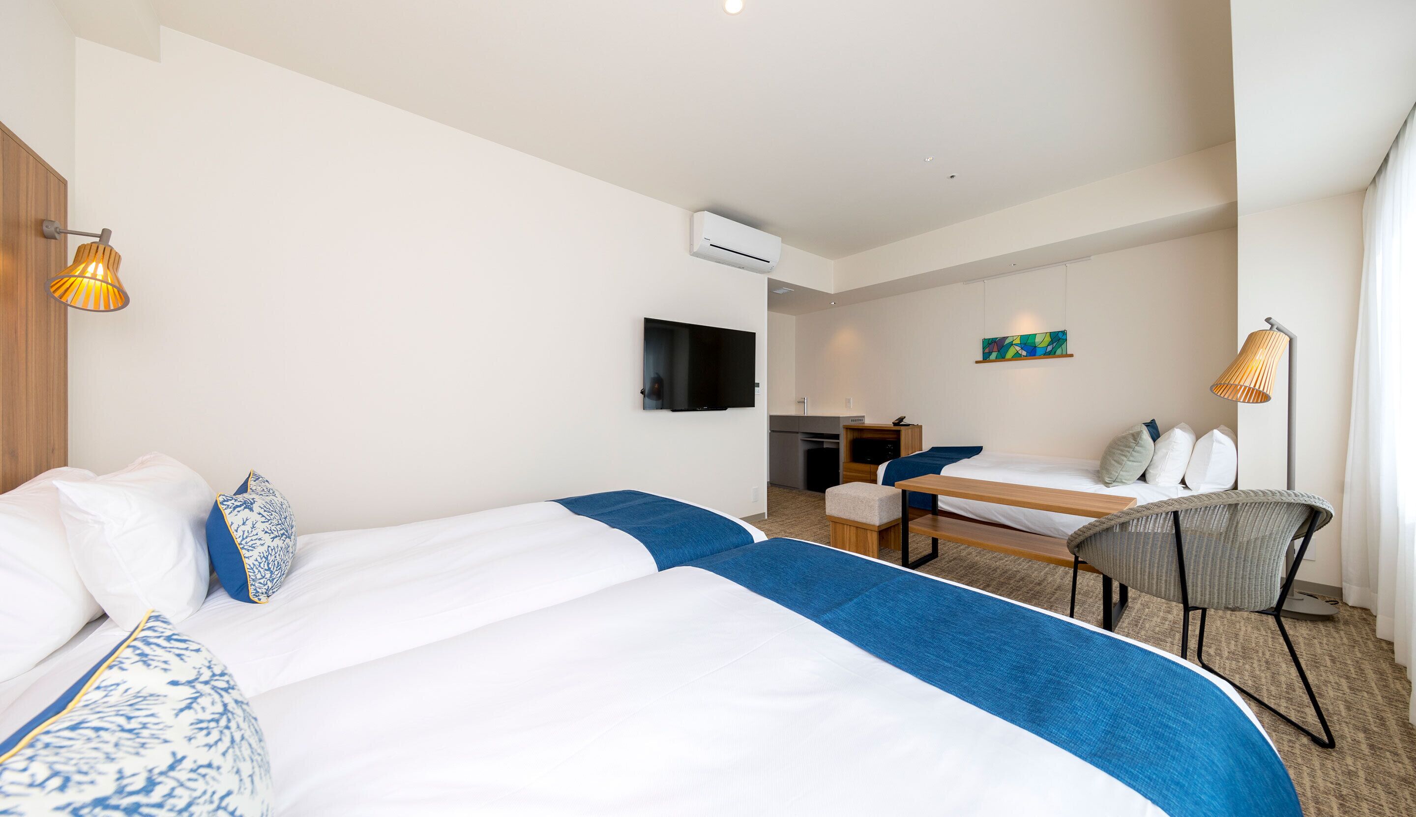 Una habitación de hotel con dos camas, un escritorio, una silla, un televisor y un equipo de aire acondicionado.