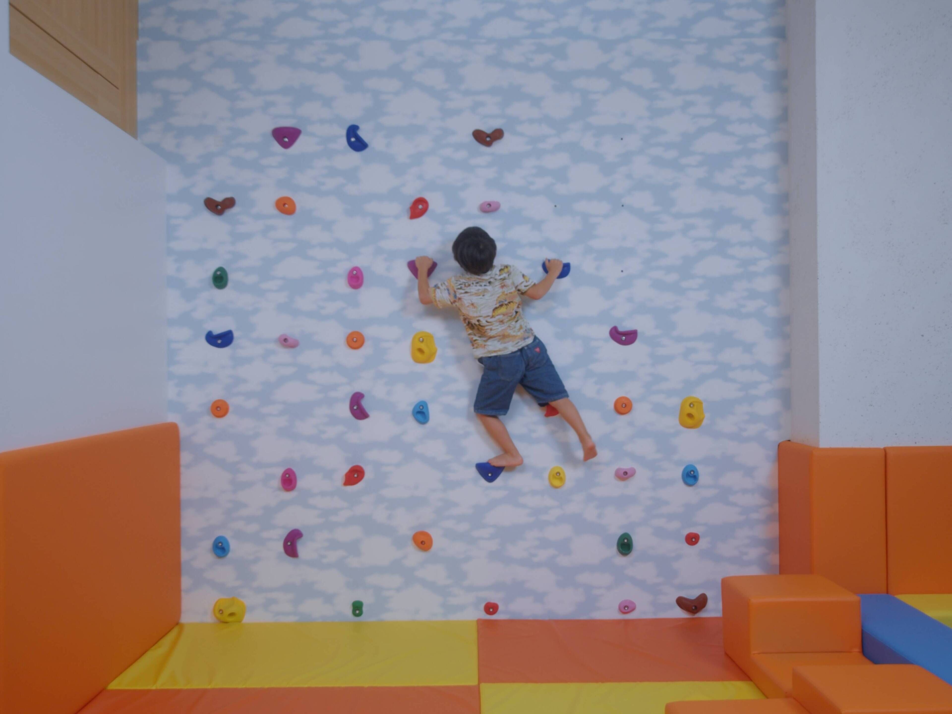 A child climbing a wall with colorful handholds.