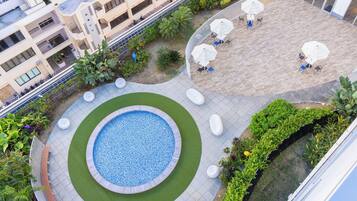 A rooftop pool area with a circular pool, surrounding seating, and a landscaped garden.