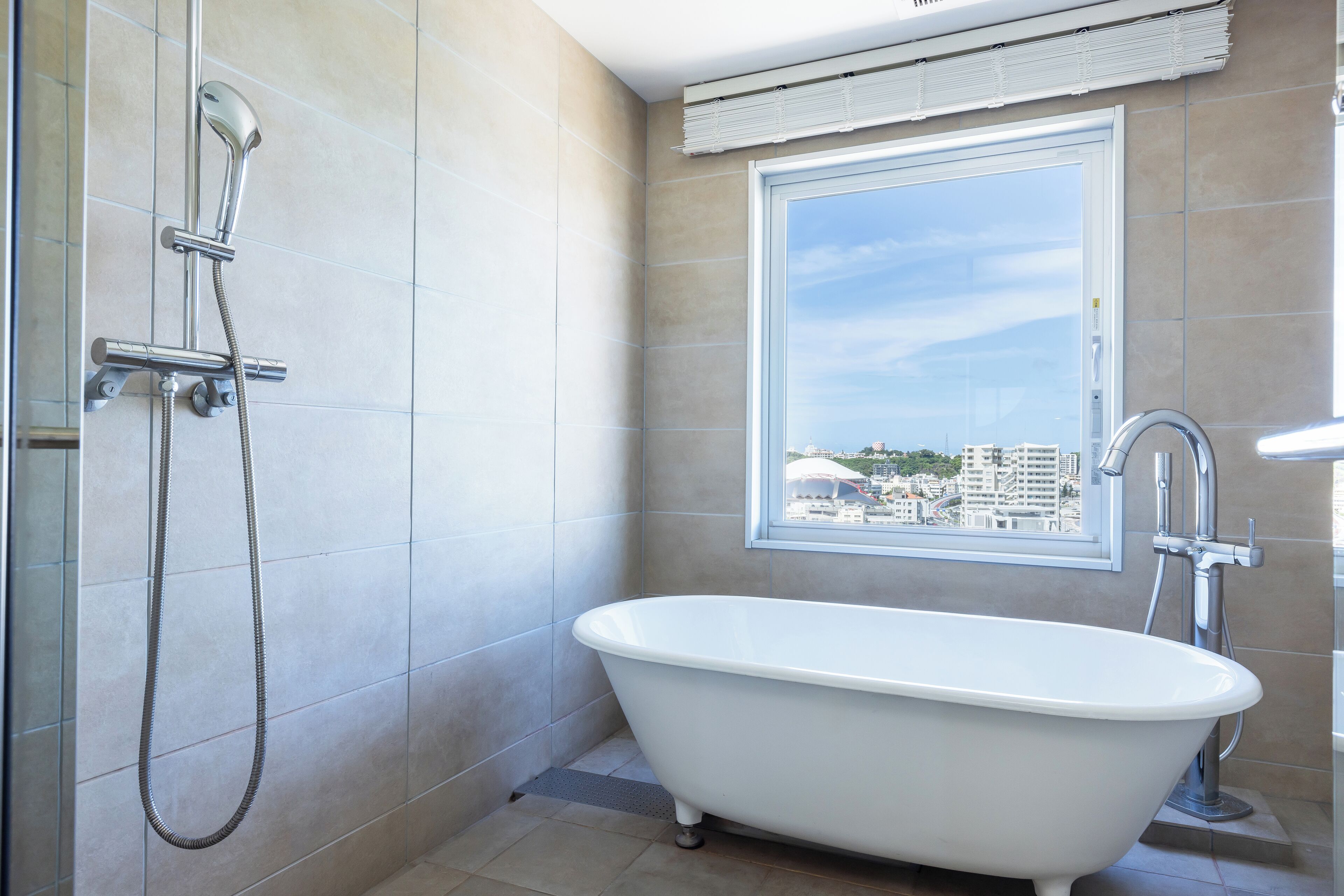 A bathroom with a bathtub, a shower, and a window with a city view.