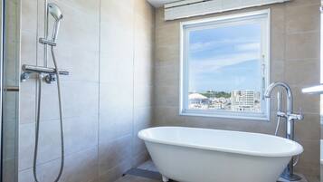 A bathroom with a bathtub, a shower, and a window with a city view.