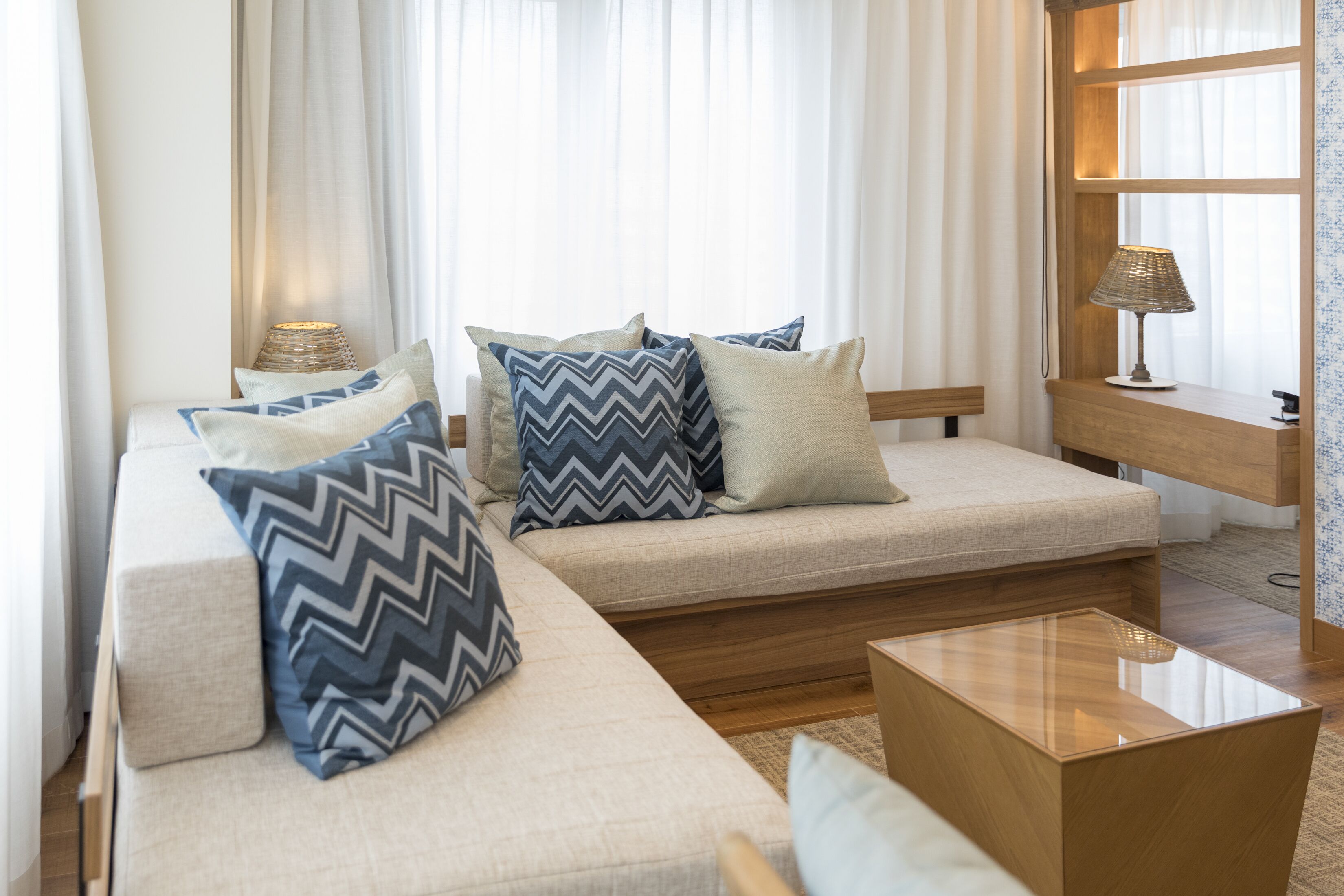 Een moderne woonkamer met een zithoek, een glazen salontafel en een lamp op een houten bijzettafeltje.