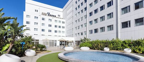 A modern hotel with a swimming pool, outdoor seating, and lush greenery.