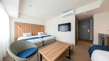 Habitación de hotel con dos camas, televisión, aire acondicionado, cabecero de madera y zona de estar con mesa y sillas.