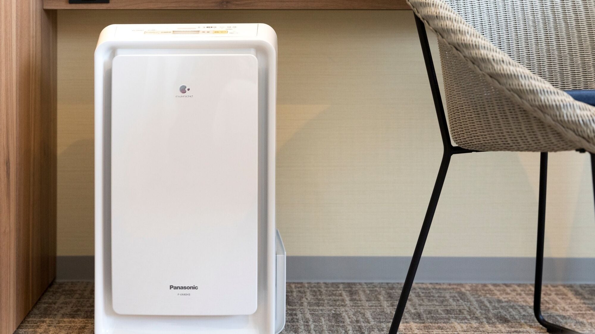 A Panasonic air purifier in a room with a chair and a wooden cabinet.