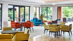 A spacious indoor area with large windows, yellow and orange chairs, a blue sofa, and a small table. - Scarman - Warwick Conferences (Coventry)