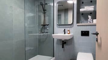 Een moderne badkamer met een douchecabine van glas, een witte wastafel en een toilet.