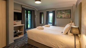 A hotel room with a large bed, a TV on a shelf, a lamp, and a painting on the wall. - Scarman - Warwick Conferences (Coventry)