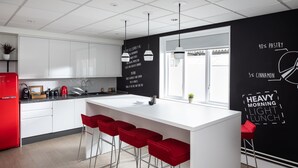 A modern kitchen with white cabinets, a red refrigerator, and a black wall with text. - Scarman - Warwick Conferences (Coventry)