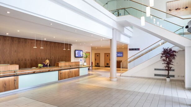 A modern hotel lobby with a reception desk, a staircase, and a large plant. - Scarman - Warwick Conferences (Coventry)